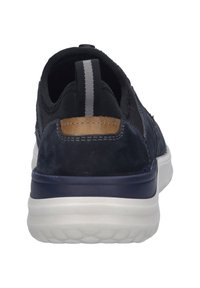 Navyblaue Sneaker mit Obermaterial aus Wildleder und Stoff, weißer gepolsterter Sohle und einem kontrastierenden braunen Akzent an der Ferse. Grauer Zuglasche auf der Rückseite.