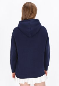Sudadera azul marino con capucha, de corte holgado, confeccionada con tela suave. Cuenta con un dobladillo y puños acanalados, con una textura sutil.