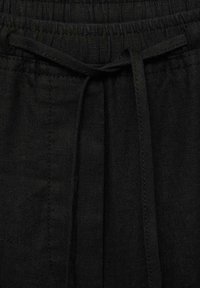 Pantalon en tissu noir avec une taille élastique et un cordon noué à l'avant au centre, montrant la texture et les détails des coutures.