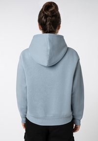 Hellblauer Fleece-Hoodie mit großer Kapuze, gerippten Bündchen und Saum. Glatte Textur, klassische Passform, schlichtes Design ohne sichtbare Muster oder Akzente.