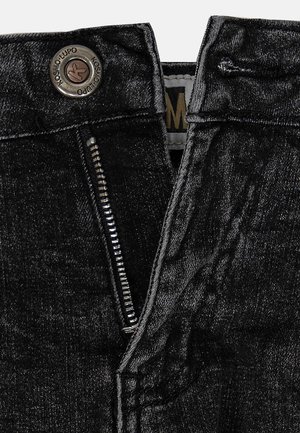 Zwarte denim jeans met een zichtbare metalen rits en drukknopen, voorzien van een gestructureerd oppervlak en contrasterende stikdetails.