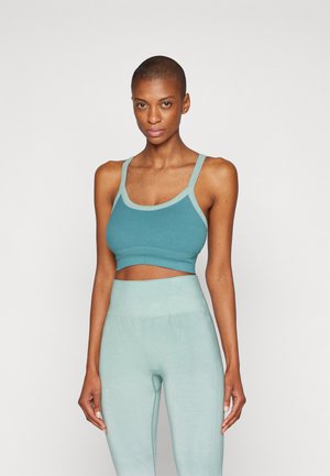 Sostenedor deportivo en color verde azulado con acentos en un tono verde azulado claro, que presenta un diseño ajustado y tirantes anchos. Combinado con leggings de talle alto a juego, con una textura suave.