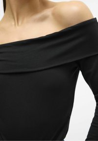 Musta olkapäältä avattu paita, joka on valmistettu pehmeästä kankaasta ja jossa on taitettu kaulus sekä istuvat hihat. Luja pinta ja klassinen muotoilu.