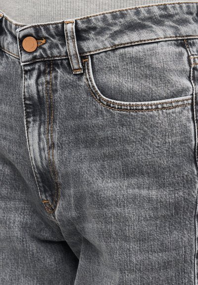 Εγγύς λήψη ξεθωριασμένου μαύρου τζιν με λεπτομέρειες μπροστινής τσέπης, κουμπιού, θηλιάς ζώνης και πορτοκαλί ραφής.