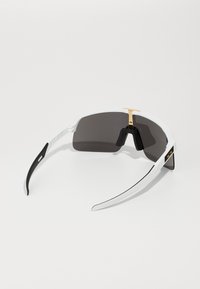 Gafas de sol con un marco blanco y negro, lentes oscuros, acento de hardware dorado en el puente y brazos curvados elegantes.