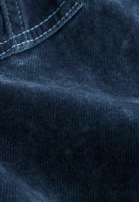 Donkerblauwe corduroy stof, met fijne ribbels en een gladde textuur, met contrasterende stiksels die de diepte en details van de stof tonen.