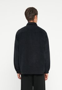 Black textured shirt with a grid pattern, long sleeves, and a collar. The fabric appears soft and has a relaxed fit.