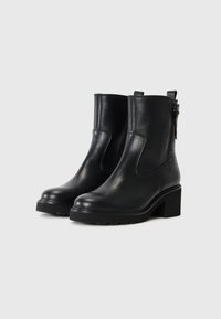 Botines de cuero negro con tacón cuadrado, textura suave, paneles laterales elásticos y cierre de cremallera en el lado exterior.
