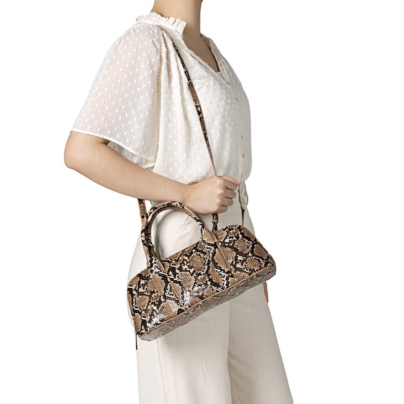 Femme portant une tenue blanche tenant un sac à main à motif cuir de serpent marron et noir avec deux poignées supérieures et une bandoulière.