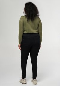 Jean skinny noirs avec un haut côtelé vert olive texturé, doté de manches longues et de détails froncés aux épaules. Accentué par des poches arrière.
