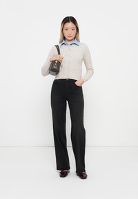 Cardigan de punto beige, camisa de cuello azul claro, jeans rectos negros y zapatos burdeos. Pequeño bolso gris llevado al hombro.