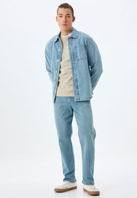 Camisa de mezclilla azul clara con un bolsillo, camiseta beige y jeans azul claros a juego. Zapatillas blancas y beige completan el atuendo.