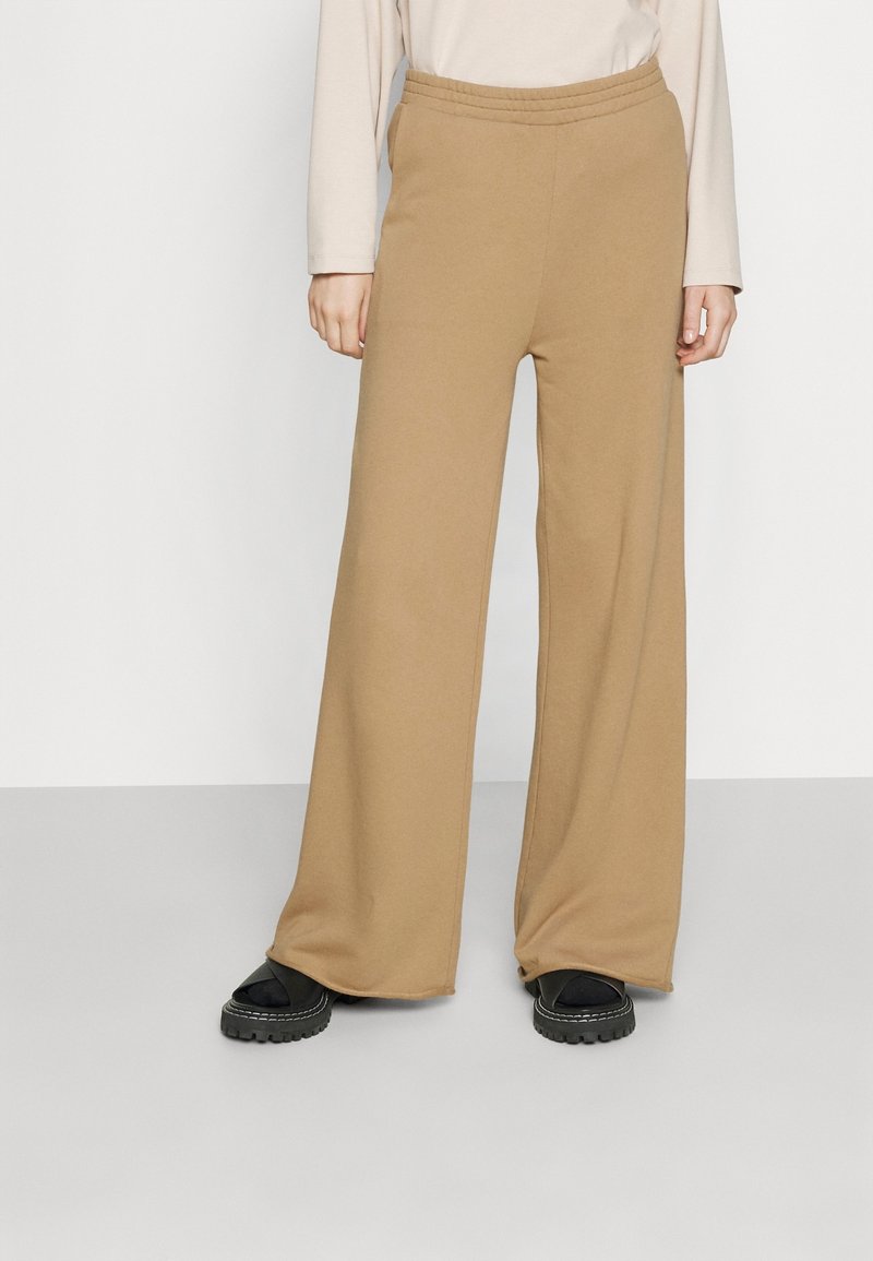 Pantalons beiges à jambe large en tissu doux, dotés d'une taille élastique et d'une coupe décontractée, portés avec des sandales à plateforme noires.