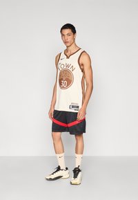 Basketbola krekls krēmkrāsā ar brūniem akcentiem, uz kura rakstīts "The KOWN" un numurs 30. Kombinēts ar melnām šortām ar sarkanām strīpām un sporta apaviem.