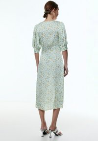 Blumen-Midi-Kleid aus hellblauem Stoff, mit Puffärmeln und tailliertem Schnitt, versehen mit einem zarten gelb-grünen Blumenmuster.