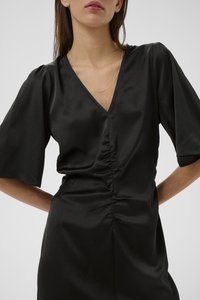 Melna kleita ar V veida izgriezumu, īsām piedurknēm, savākumu pie vidukļa un gludā zīda līdzīgā faktūrā. Vienkāršs sudraba ķēdītes kaklarota.