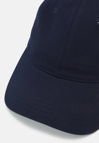 Boné de basebol azul-marinho feito de algodão, com aba curvada, detalhes costurados e uma coroa arredondada com orifícios de ventilação.