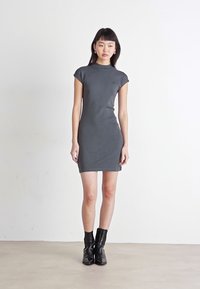 Γκρίζα βαμβακερή φόρεμα με κοντά μανίκια, στρογγυλή λαιμόκοψη και ευθεία σιλουέτα, συνδυασμένο με μαύρες μπότες έως τον αστράγαλο. Λείος υφασμάτινος χαρακτήρας.