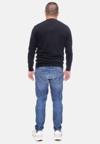 Maglione nero, jeans blu e sneakers bianche. Design semplice; maglione a maniche lunghe, jeans leggermente affusolati, dettagli delle tasche visibili sul retro.