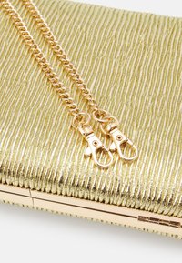 Złota metaliczna kopertówka o teksturowanej powierzchni, z złotą łańcuszkową rączką i klamrą. Płaski design z gładkim zapięciem na zamek.