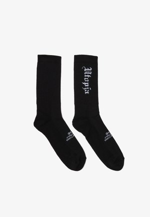 Coppia di calzini neri a coste, con testo bianco "Wacko Maria" sull'area del polpaccio e piccolo testo bianco vicino alle dita dei piedi.