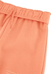 Joggers color pesca con vita elastica, cordino e tessuto texturizzato. Presentano un piccolo logo e del testo stampato vicino all'orlo.