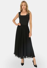 Czarna sukienka bez rękawów o kwadratowym dekolcie, zwiewna spódnica i dopasowany gorset. Połączona z czarnymi szpilkami z ozdobnym wykończeniem.