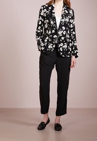 Svart blommig kavaj med vita blommor, slagkragar, två framfickor, kombinerat med svarta tapered-byxor och svarta loafers.