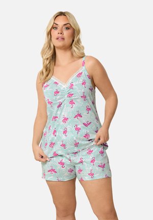 Mujer con un conjunto de pijama sin mangas con estampados de flamencos rosas y hojas verdes sobre un fondo azul claro.