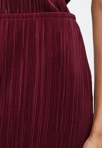 Βουργουνδί φόρεμα με πτυχώσεις, κατασκευασμένο από υφασμάτινη επιφάνεια, με ελαστική μέση και κατακόρυφες αυλακώσεις για ρέουσα σχεδίαση.