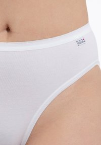 Weißer Baumwollslip mit einem weichen, elastischen Bund. Nahtlose Kanten und ein kleines Logoetikett an der Seite. Glatte Textur, figurbetontes Design.