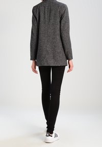 Svarta slim-fit jeans tillsammans med en texturerad grå blazer. Blazern har långa ärmar och en ren, minimalistisk design. Vita sneakers med svarta ränder.