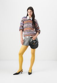 Dugini pletena sweater, siva plisirana suknja, žute tajice, crne cipele s potpeticom i crna torba sa čavlima.