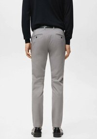 Pantaloni grigi su misura con una texture liscia, dotati di due tasche posteriori, abbinati a una cintura nera e a scarpe eleganti nere.