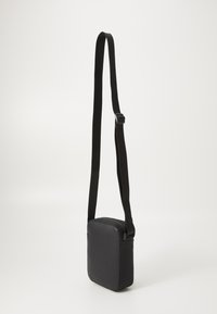 Schwarze Umhängetasche aus glattem Material, rechteckige Form, verstellbarer Riemen, Reißverschlussverschluss und minimalistisches Design.