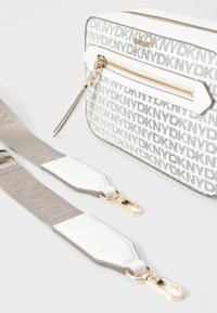 Borsa bianca con motivo a logo grigio ripetuto, hardware dorato e chiusura con zip. Include una tracolla staccabile grigia con dettagli bianchi.