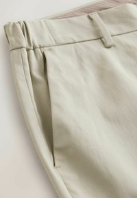 Pantaloni in tessuto beige chiaro con superficie testurizzata, dotati di una vita e pence per una vestibilità ottimale. Senza hardware o motivi visibili.