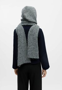 Grijze wollen sjaal en capuchon set, met een zachte, gestructureerde afwerking en ruwe randen, gedrapeerd over een donkere jas, aangevuld met gestreepte broek.