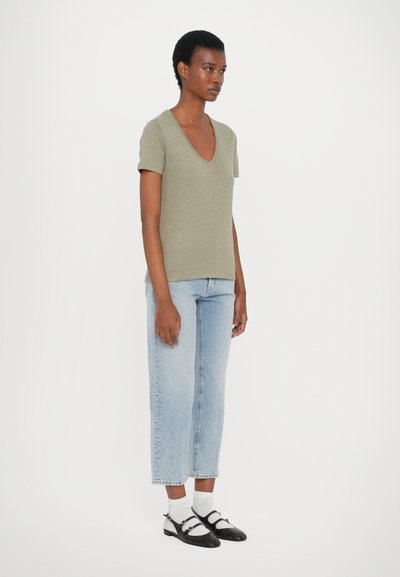 Olivgrön t-shirt med v-ringning kombinerad med ljusblå avslappnade jeans och svart-vita tvåtonsskor med ankelsnöre.