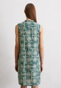 Ärmlös grön klänning med vit geometrisk cirkelformad mönster, tillverkad av ett mjukt tyg, knälång design.