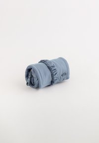 Bolsa enrollable de tela azul acolchada con un acento elástico recogido, cierre con cremallera y un sutil detalle de costura. Forma compacta y cilíndrica.