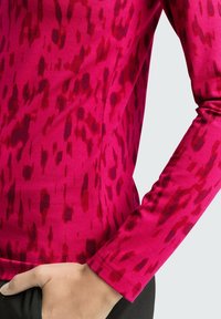 Enganliegendes Langarmoberteil in leuchtendem Pink mit einem strukturierten Muster aus dunkleren roten Punkten, aus weichem, dehnbarem Stoff gefertigt.