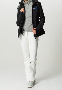 Svart softshell-jacka med huva, grå polo-krage, och vita byxor, med dragkedjefickor och en avslappnad passform. Skorna är ljusgrå.