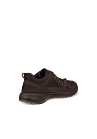 Chaussure de sport marron en matériaux mesh et daim, avec une semelle texturée, des lacets jaunes et un design élégant agrémenté d'accents décoratifs.