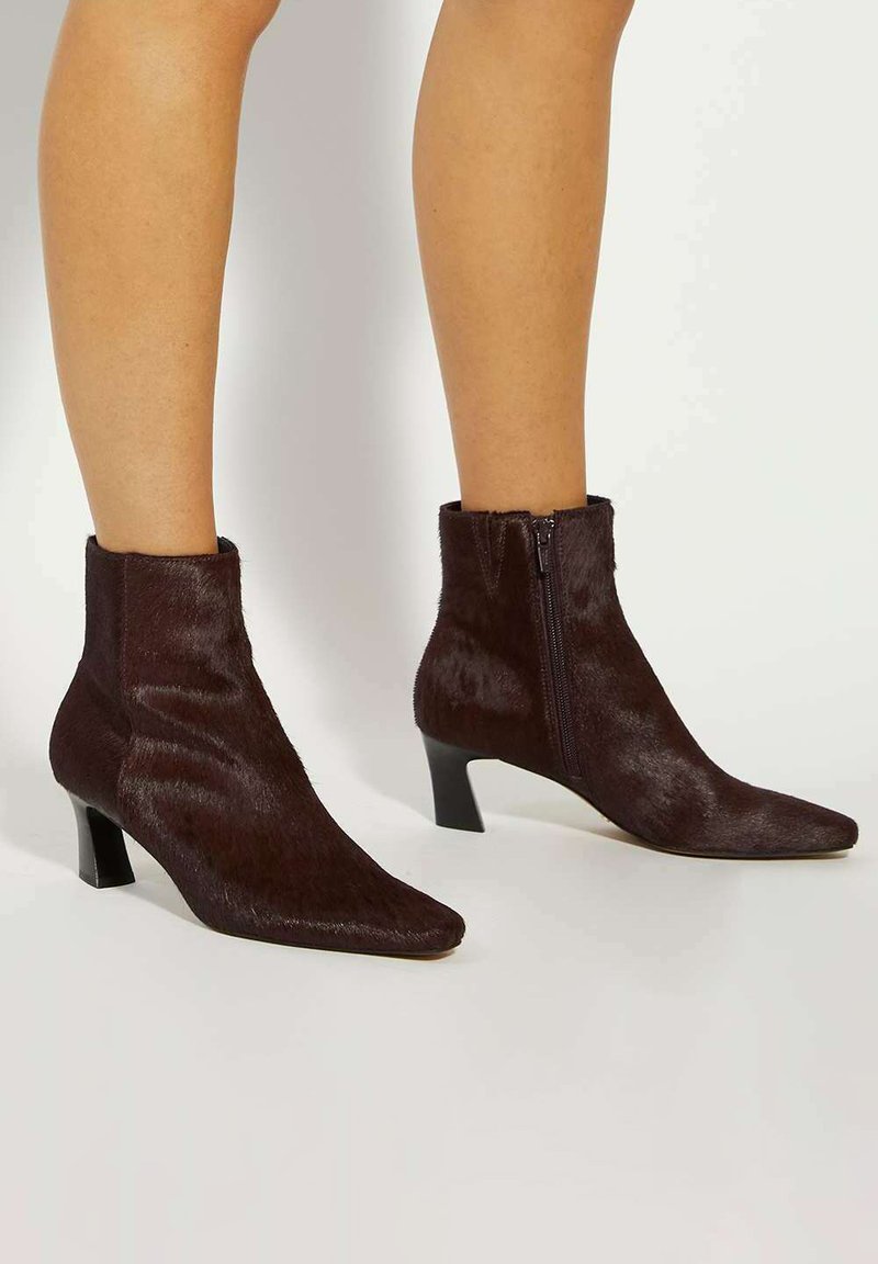 Brown faux fur ankle boots with a pointed toe, low block heel, and side zipper detail. Smooth texture with a fitted silhouette.