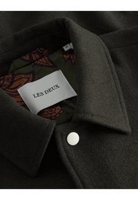 Giubbotto di lana grigio scuro con colletto a ribalta, dotato di una fodera verde vivace e decorata. Presenta un'etichetta bianca con la scritta "LES DEUX."