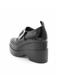 Zwarte lakleren schoen met een chunky platform en hak, voorzien van een zilveren gesp aan de zijkant en een gladde, glanzende textuur.