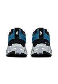 Chaussures de sport bleues et noires avec une tige en maille, une semelle blanche proéminente et un onglet au talon noir avec un logo et des détails textuels.