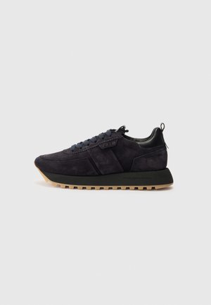 Baskets noire en daim à lacets, avec une épaisse semelle intermédiaire noire et une semelle extérieure beige à reliefs, présentée de profil sur un fond uni.