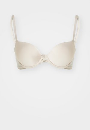 Soutien-gorge beige avec des bonnets moulés lisses, des bretelles réglables et une bande latérale texturée. Il dispose d'une fermeture centrale à crochet et d'un design sans couture.